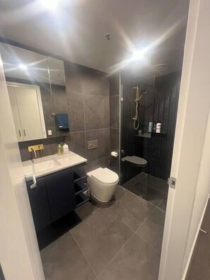 Un baño moderno con un espejo grande, inodoro, lavabo y zona de ducha.