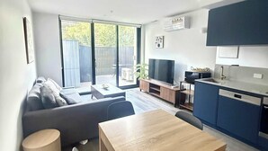 A modern living space with a sofa, a dining table, a kitchen area, and a sliding glass door leading to an outdoor area. - CBD | Pool | Sleeps 4 | Parking | Pets (Reid)