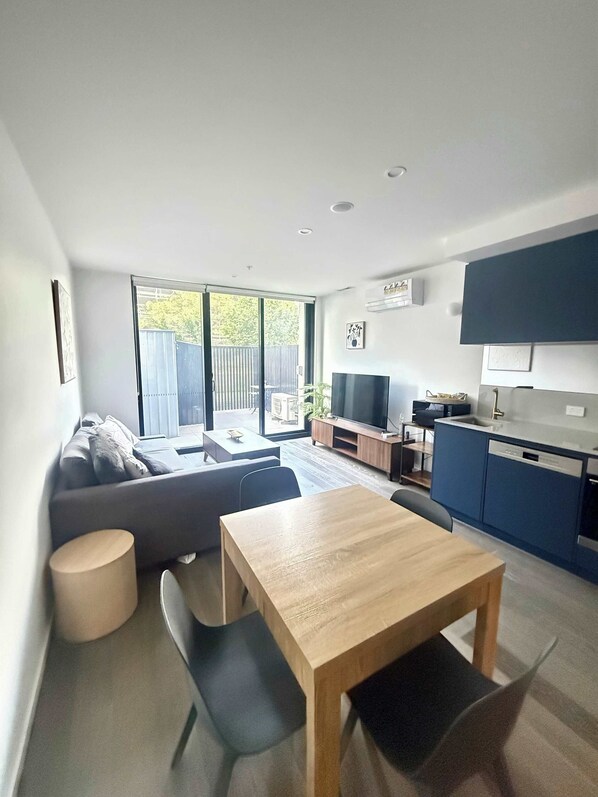 Un espacio habitable moderno con sofá, una mesa de comedor, una zona de cocina y un ventanal corredero que da a un área exterior.