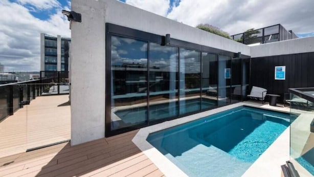 A rooftop swimming pool with glass walls, a wooden deck, and a city view. - CBD | Pool | Sleeps 4 | Parking | Pets (Reid)