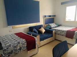 Una habitación con tres camas, cada una con un diseño diferente de cabecera. Hay un escritorio y una silla en el centro de la habitación.