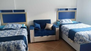 A bedroom with two beds, a nightstand, and a blue sofa. - MADEII project training center hostel (Al-'Amriyah)