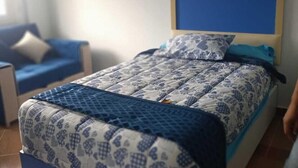 A bedroom with a bed, a blue headboard, and a patterned bedspread. - MADEII project training center hostel (Al-'Amriyah)