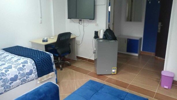 A room with two beds, a desk with a computer, a TV mounted on the wall, and a refrigerator. - MADEII project training center hostel (Al-'Amriyah)