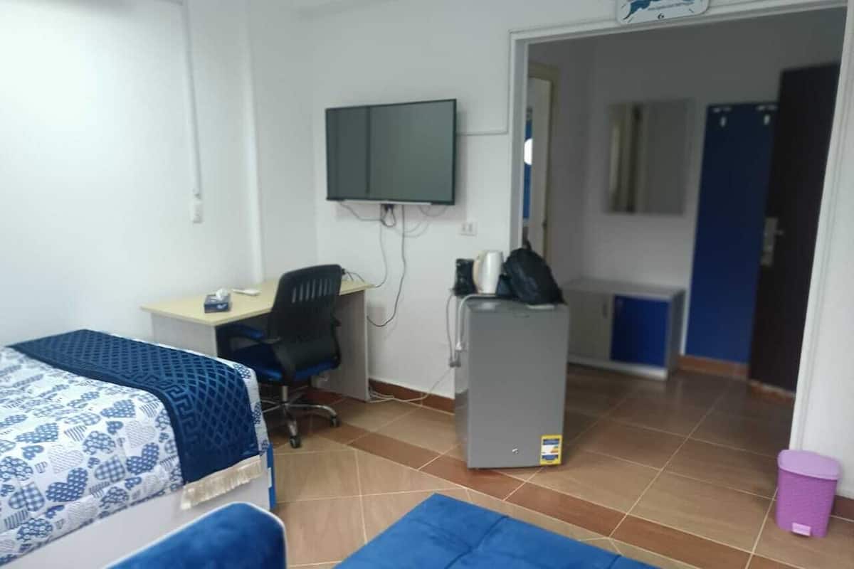 Ein Zimmer mit zwei Betten, einem Schreibtisch mit Computer, einem an der Wand montierten Fernseher und einem Kühlschrank.