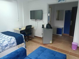 Una habitación con dos camas, un escritorio con computadora, un televisor montado en la pared y un refrigerador.