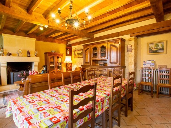 Une salle à manger avec une longue table, des chaises en bois, un lustre, une cheminée et un buffet aux portes vitrées.