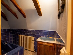 A bathroom with a bathtub, a sink, a radiator, and wooden beams on the ceiling.