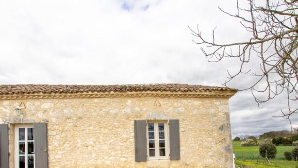 A stone building with a tiled roof, a door with shutters, and a window with shutters.