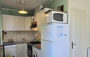 Une cuisine compacte avec des meubles blancs, un four à micro-ondes, un réfrigérateur, une cuisinière et un luminaire suspendu.