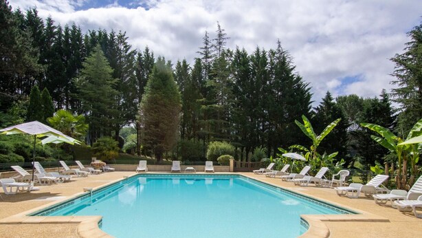 A rectangular swimming pool with a pebble-lined edge, surrounded by white lounge chairs and umbrellas. - Charming house in Prats-du-Périgord with enclosed garden (Prats-du-Périgord)