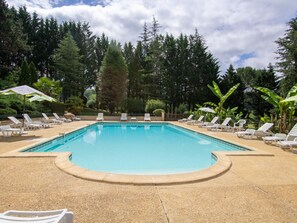 Una piscina rectangular con borde de guijarros, rodeada de sillas de descanso y sombrillas blancas.