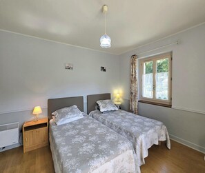 Een slaapkamer met twee bedden, een raam met gordijnen, een bedlampje en een radiator.