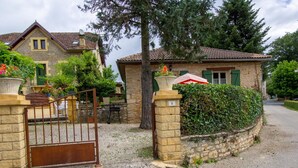 A stone house with a gated entrance, surrounded by greenery and a gravel driveway. - Charming house in Prats-du-Périgord with enclosed garden (Prats-du-Périgord)