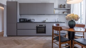 A modern kitchen with grey cabinetry, a built-in oven, a microwave, and a dining area with a wooden table and chairs.