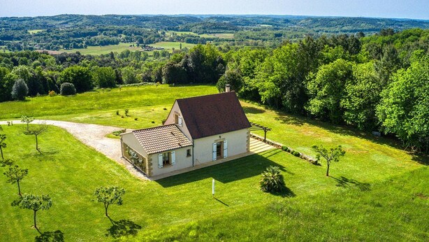 Une maison avec un toit rouge, entourée d’une pelouse bien entretenue et d’arbres, située dans un paysage rural.