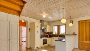 Une cuisine de taille réduite avec des meubles blancs, un îlot central et un plafond en bois.