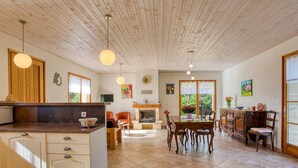 Une cuisine spacieuse dotée d’un îlot central, un coin repas avec une table et des chaises en bois, et une cheminée.