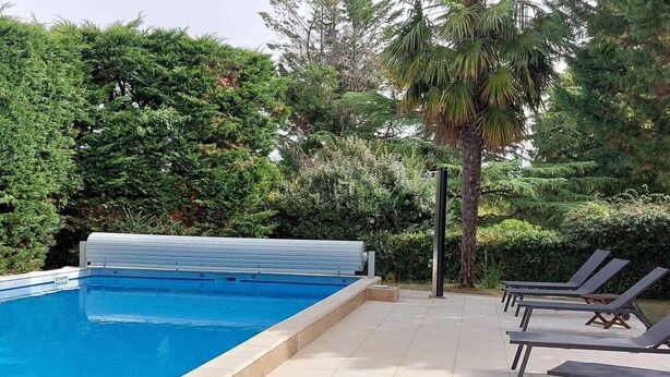 A swimming pool with a cover, surrounded by lounge chairs and lush greenery. - Charming Cottage with Pool, Near Vineyards and Historic Towns (Ginestet)