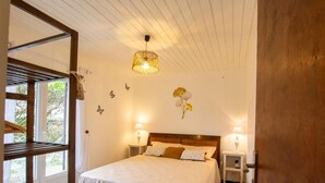 A bedroom with a bed, two bedside lamps, a wooden headboard, a window with a view, and a door.