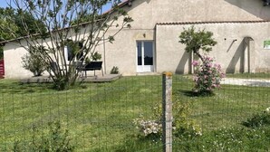 Un edificio con una puerta, un banco y un patio cercado con césped y un árbol.
