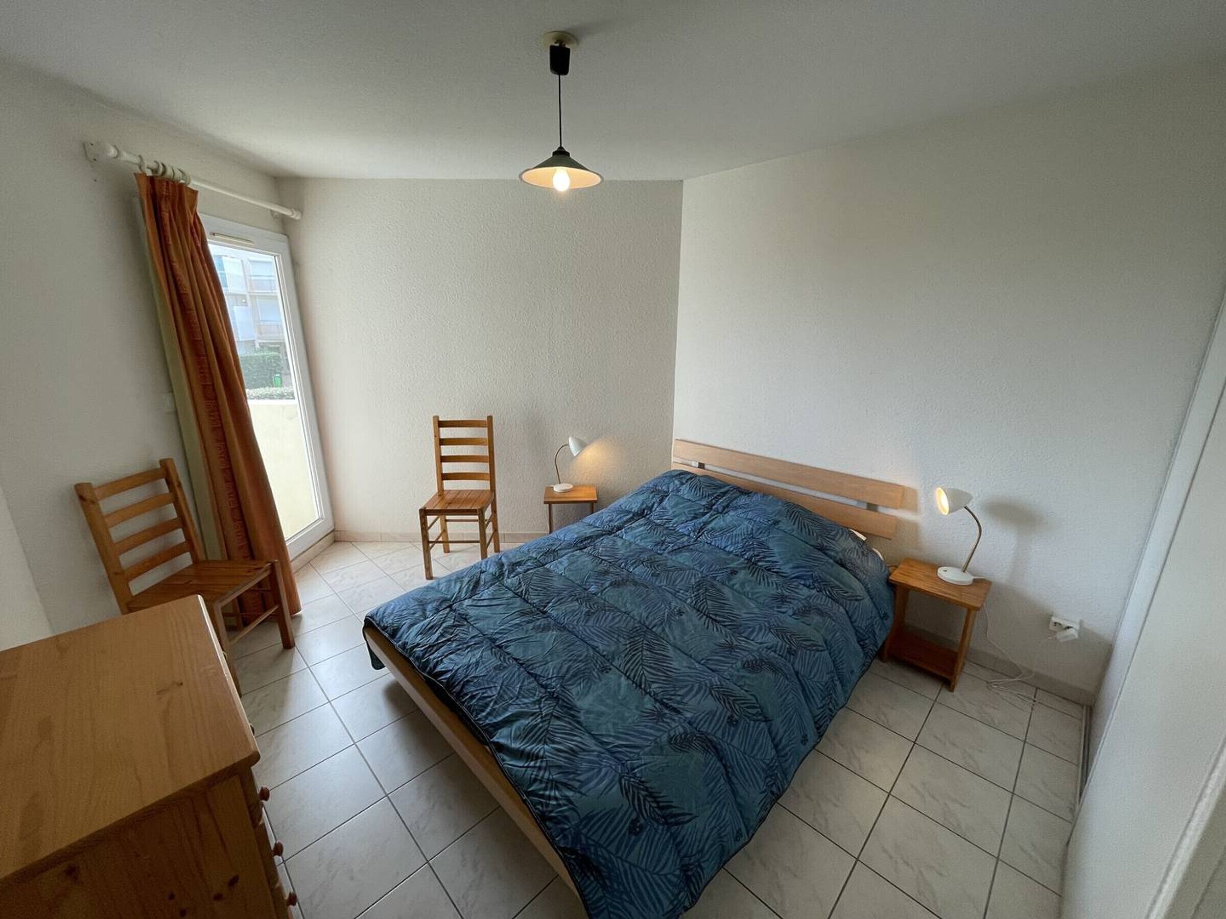 Une chambre à coucher avec un lit, deux chaises, un bureau, une lampe et un luminaire au plafond.