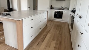 Una cocina moderna con armarios blancos, una isla central con cajones, horno integrado y una campana extractora negra.
