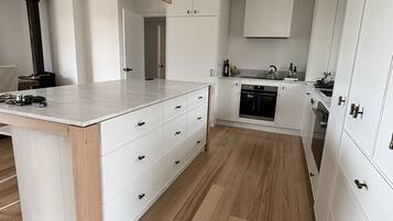 A modern kitchen with white cabinetry, a central island with drawers, a built-in oven, and a black range hood.