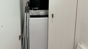 Un lavadero pequeño con lavadora y secadora, un ventanal y una puerta con picaporte de metal.