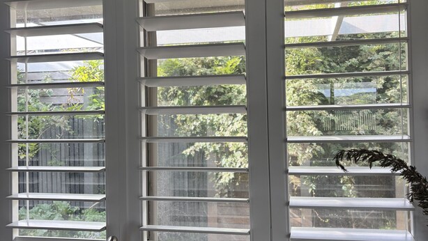 Una habitación con un ventanal grande con persianas horizontales, una encimera de mármol y un grifo moderno.