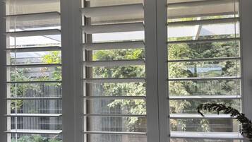 A room with a large window featuring horizontal blinds, a marble countertop, and a modern faucet.