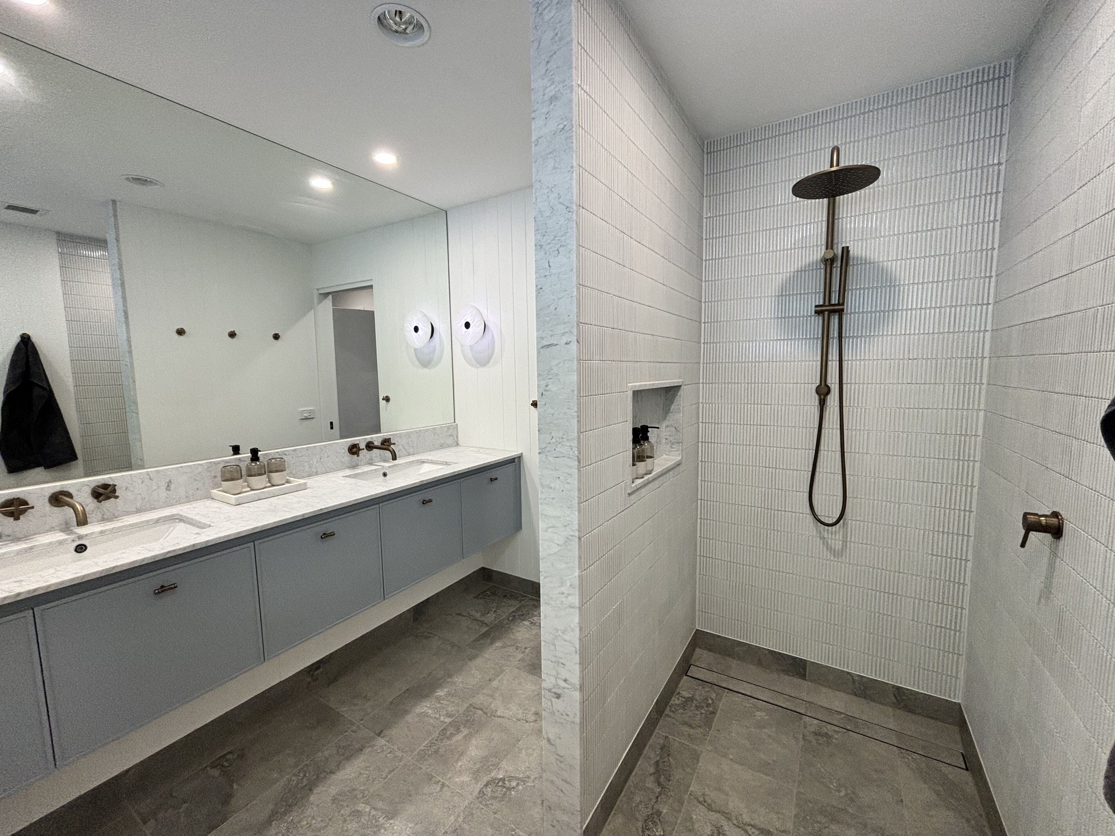A modern bathroom with a large mirror, a sink with two faucets, a shower with a handheld showerhead, and a towel rack.