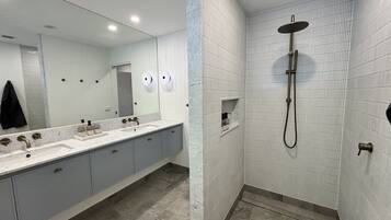 A modern bathroom with a large mirror, a sink with two faucets, a shower with a handheld showerhead, and a towel rack.