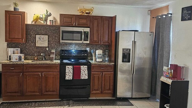 A kitchen with wooden cabinets, a stainless steel refrigerator, a microwave, and a stove.