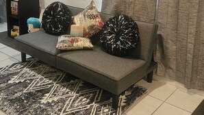 A living room with a sofa, a coffee machine, a mirror, and a patterned rug.