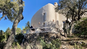 Un edificio blanco de forma abovedada con base de piedra, rodeado de árboles y vegetación.