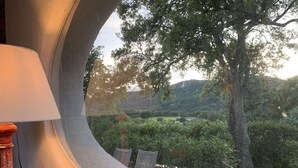 Una ventana curva con vistas a un paisaje exuberante, que incluye árboles y colinas.