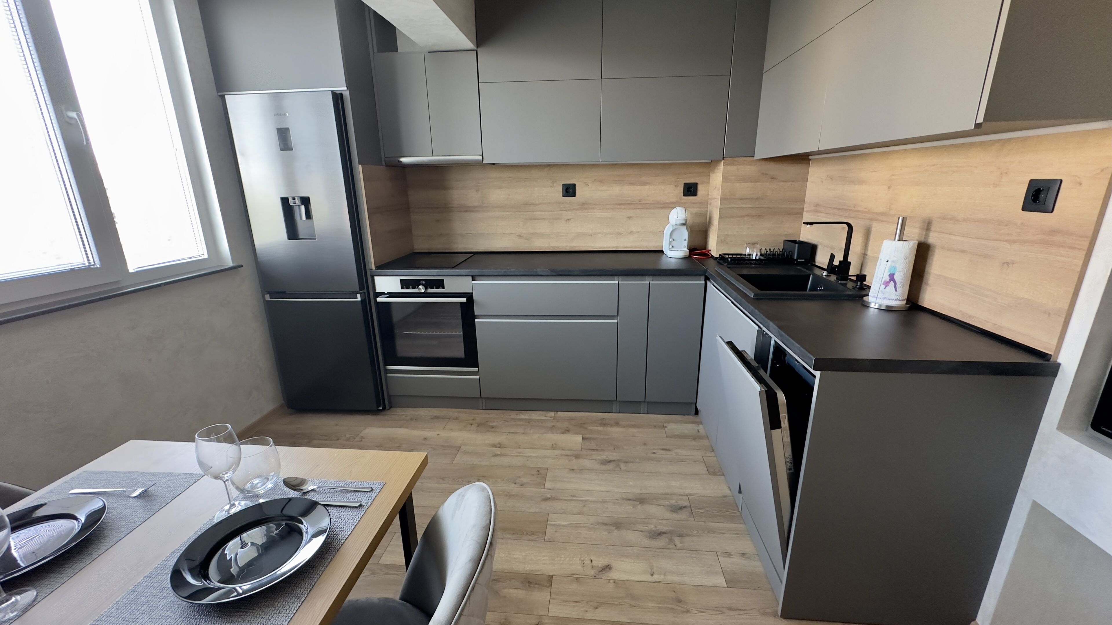 A modern kitchen with grey cabinets, a stainless steel refrigerator, a built-in oven, and a black countertop.
