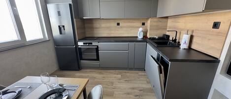 A modern kitchen with grey cabinets, a stainless steel refrigerator, a built-in oven, and a black countertop.