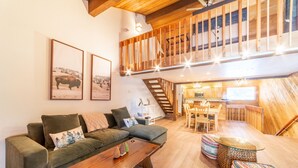 A spacious living area with a wooden staircase, a sofa, a coffee table, and a dining area. - Cozy 2+Loft in Snowcreek Meadow w/ Mountain Views! (Mammoth Lakes)