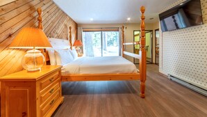 A bedroom with a wooden bed, two bedside lamps, a nightstand, and a large window. - Cozy 2+Loft in Snowcreek Meadow w/ Mountain Views! (Mammoth Lakes)