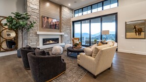 A spacious living room with a stone fireplace, large windows, and a view of the mountains. - Red Ledges luxury escape, golf, min 90 day stay (Heber City)