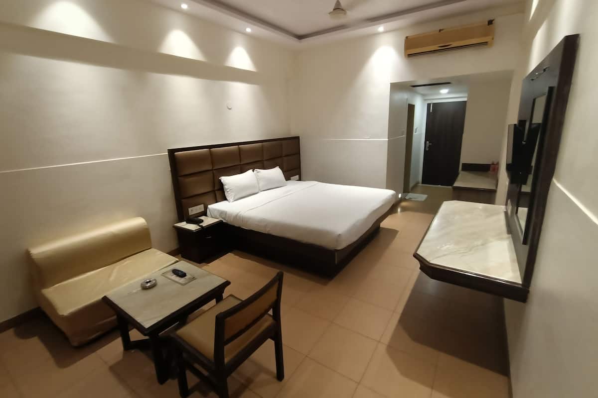 Quarto de hotel com cama, mesa de cabeceira, cadeira, escrivaninha e um espelho grande.
