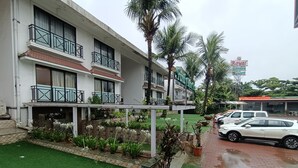 Un hotel con varios balcones, un jardín con plantas en macetas y un estacionamiento con automóviles.