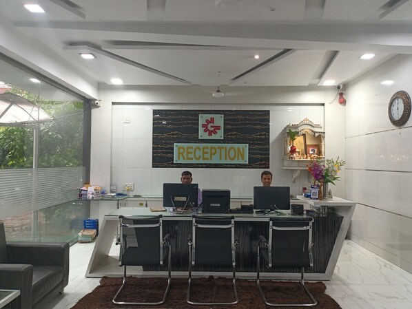 Zona de recepción con mostrador, dos monitores de ordenador, un reloj y cartel de recepción.