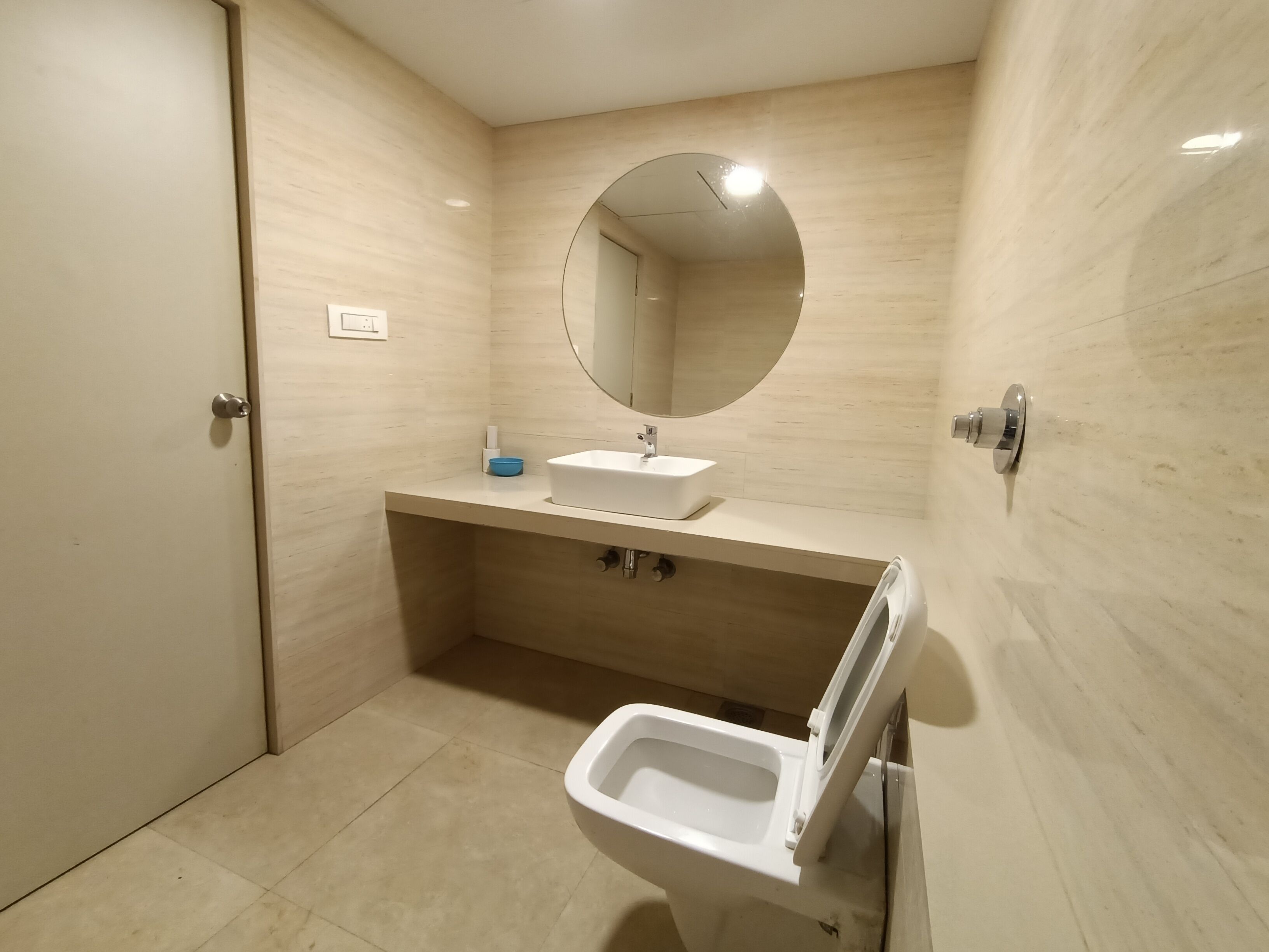 A modern bathroom with a white sink, a round mirror, and a toilet.