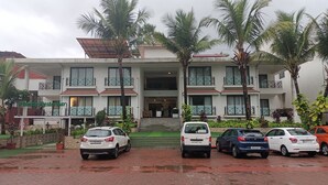 Un hotel de varios pisos con entrada central, balcones y un estacionamiento con varios automóviles.