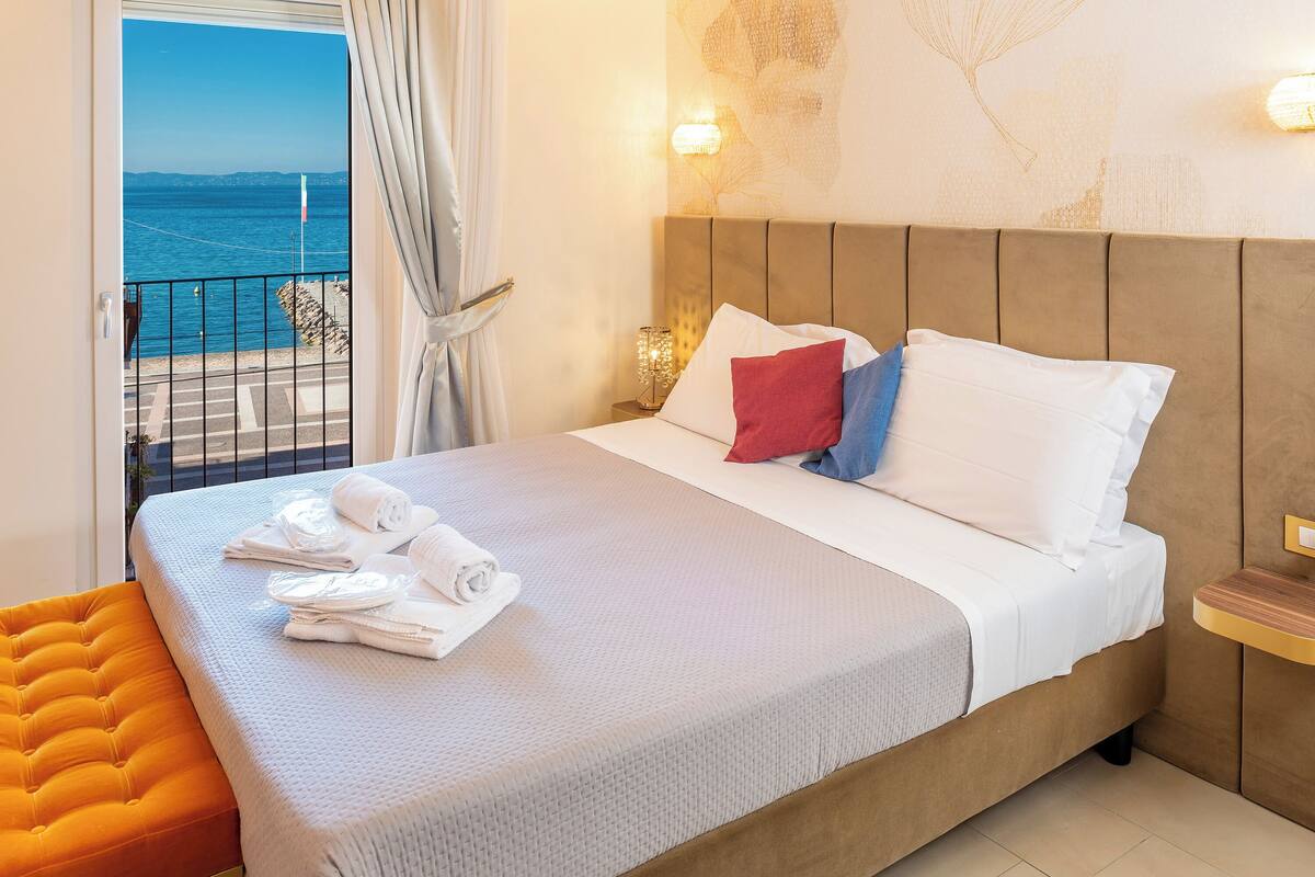 A hotel room with a bed, a view of the sea, and a balcony.