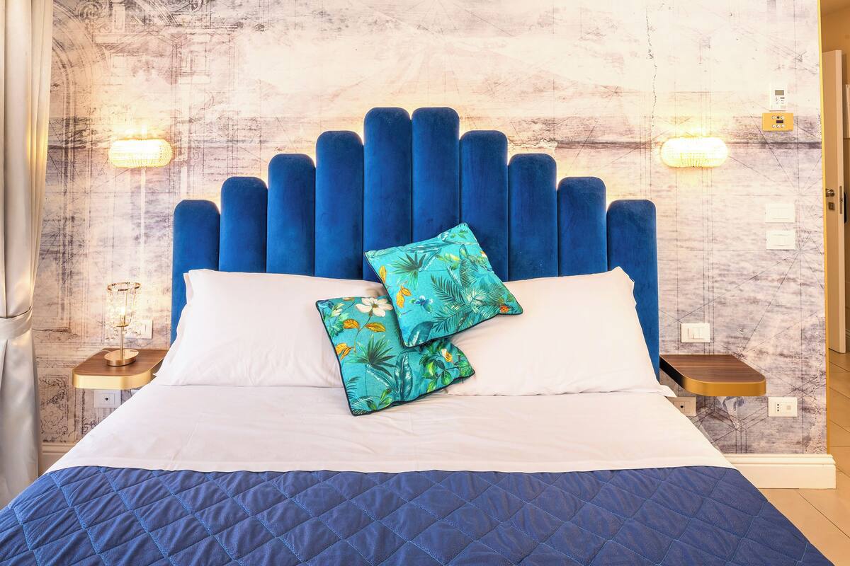 A bed with a blue headboard, white pillows, and a quilted blue bedspread. There are two bedside tables with lamps and a wall with a textured pattern.