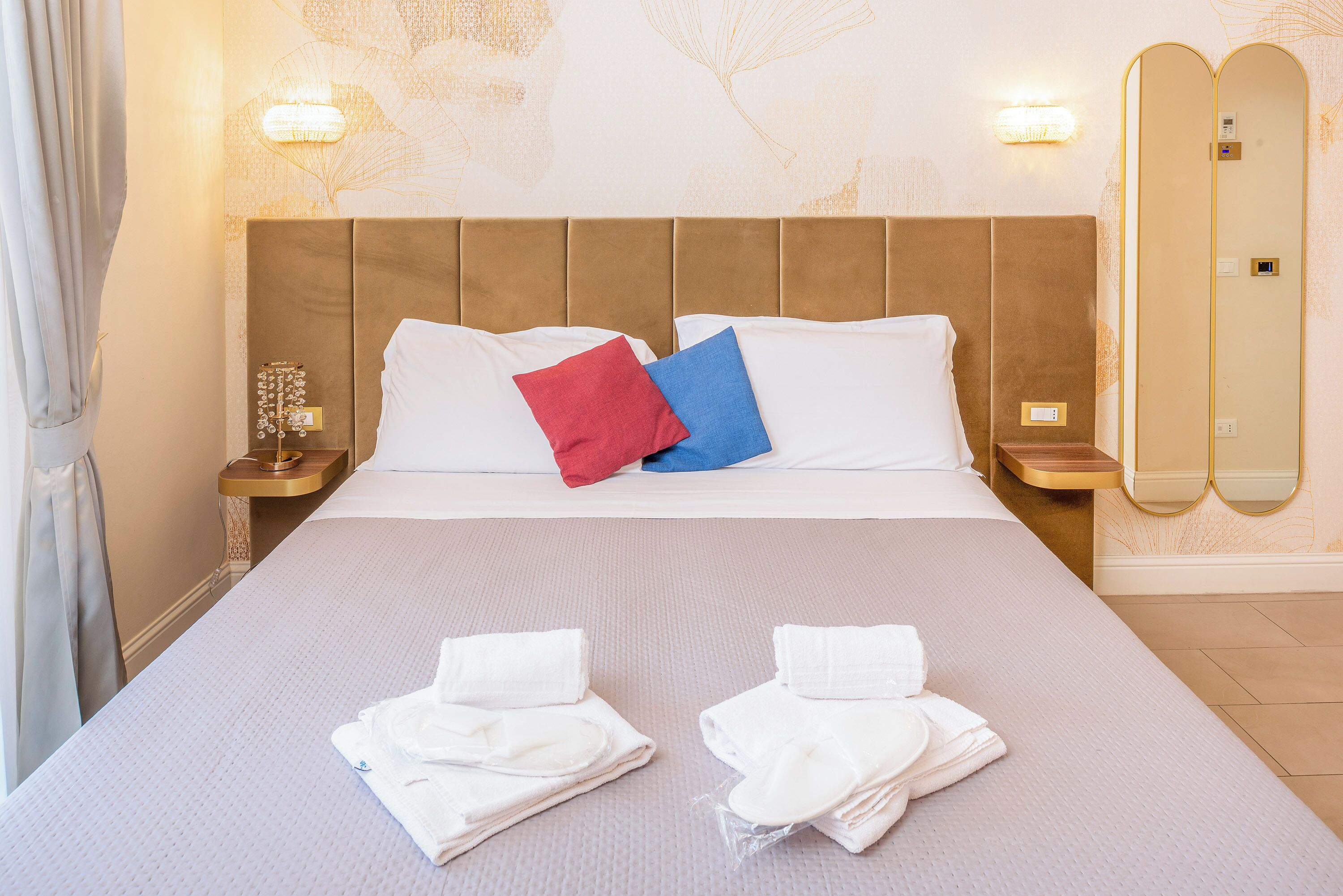 A hotel room with a large bed, two bedside tables, a mirror, and a wall-mounted light fixture.
